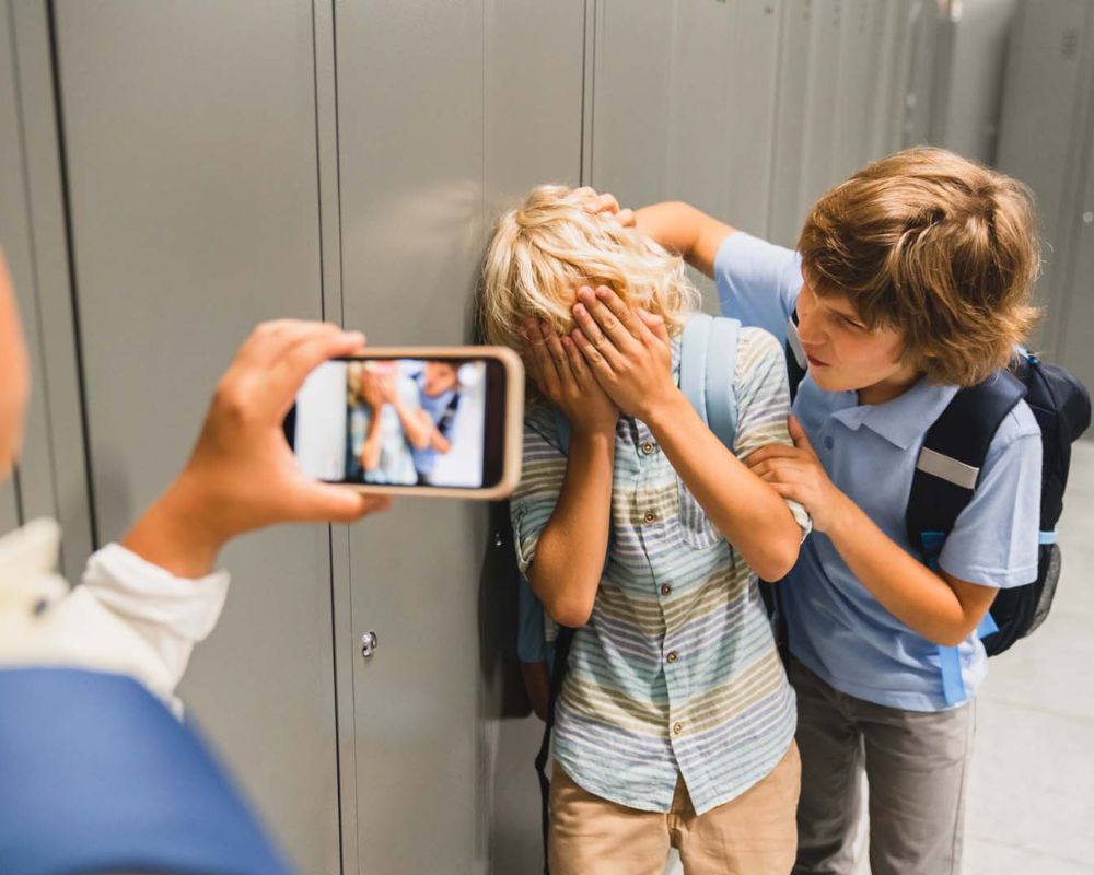 Niño siendo víctima de acoso escolar mientras es grabado con un móvil, simbolizando la necesidad de protección legal para menores.