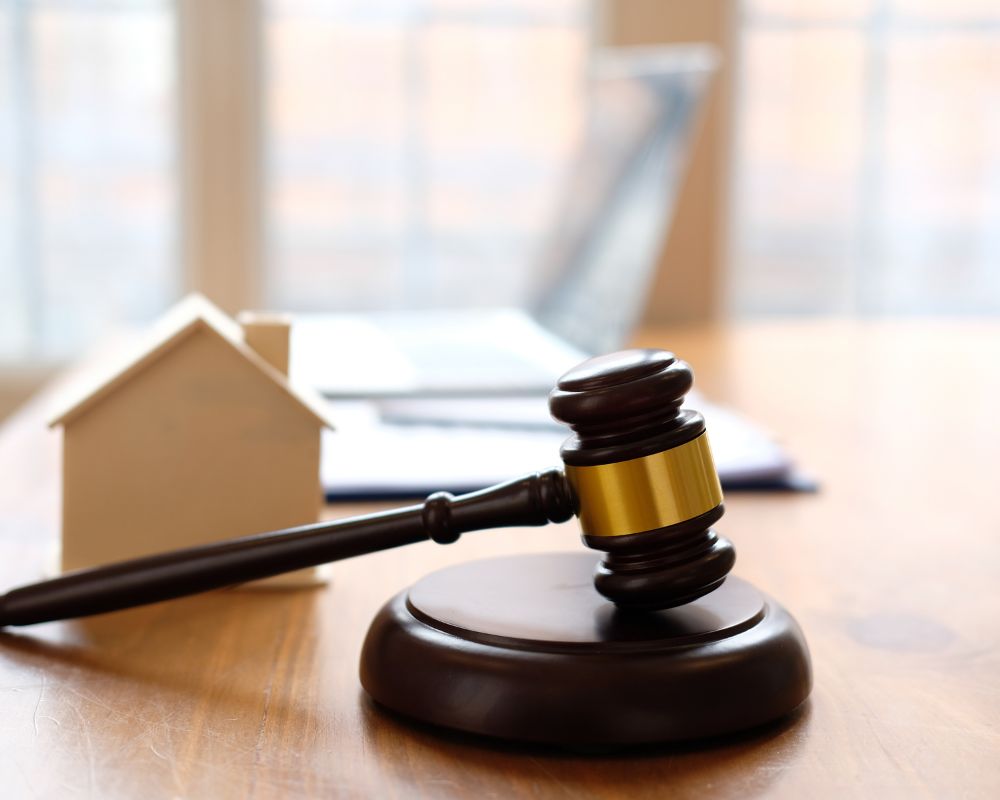 Mazo de juez junto a una casa en miniatura, simbolizando asesoramiento legal en derecho inmobiliario, testamentos y herencias.